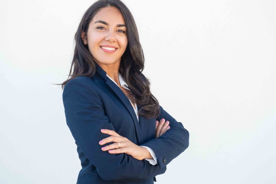 Smiling confident businesswoman posing with arms folded. Happy beautiful black haired young Latin woman in formal suit standing for camera over white studio background. Corporate portrait concept