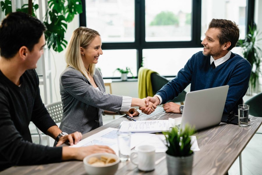 Young happy couple meeting with financial advisor in the office. Woman is handshaking with the agent.